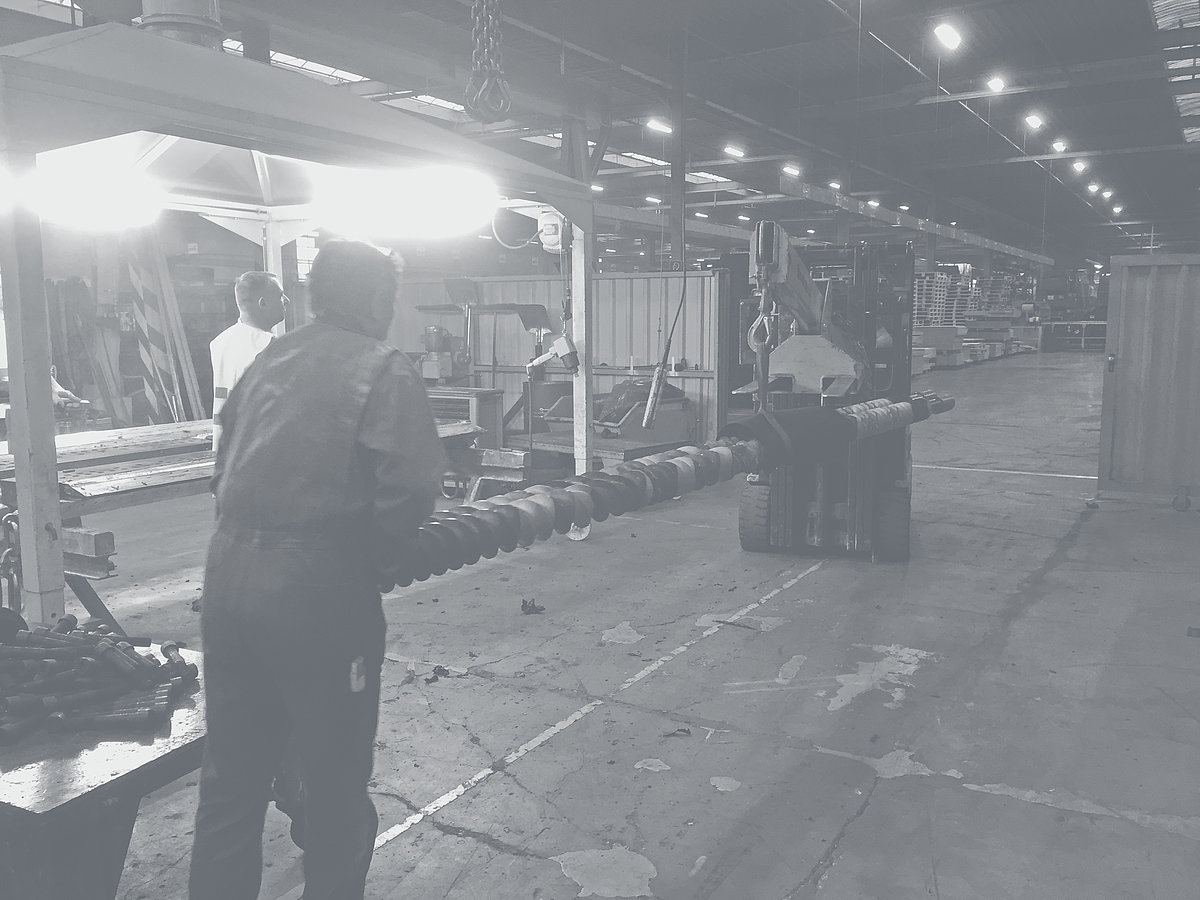 Un chariot élévateur à fourche transportant des arbres porteurs avec des éléments à travers un hall d'usine.